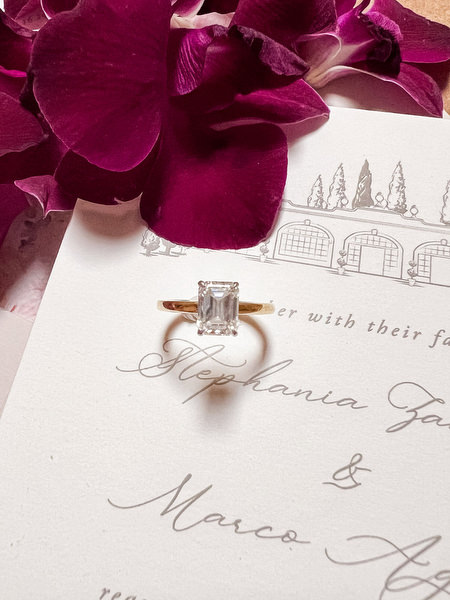 Emerald-cut engagement ring on custom wedding invitation with deep burgundy orchids for a luxury Tuscany wedding