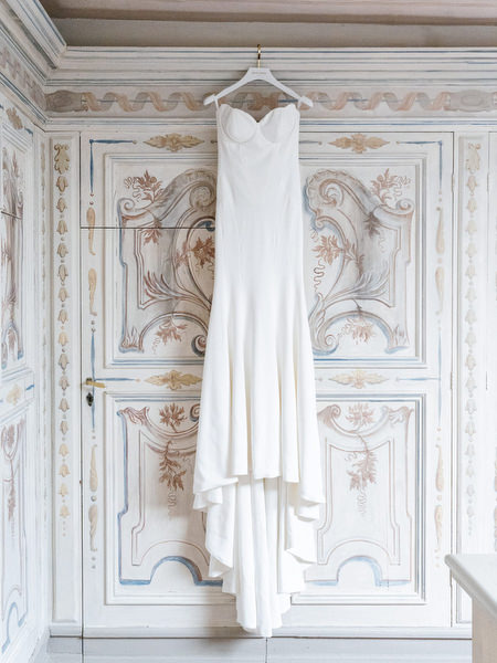 Minimalist wedding gown hanging against ornate hand-painted doors at La Foce in Tuscany