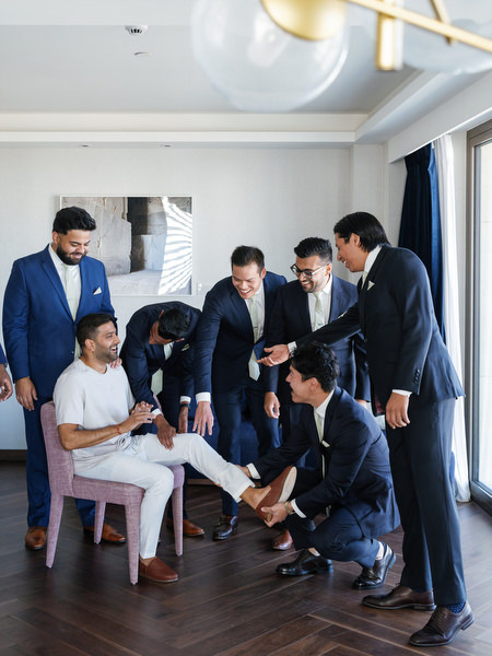 Groomsmen helping the groom dress in traditional sherwani during an Athens Riviera Indian wedding at Island Art & Taste