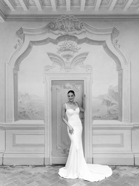 Full-length bridal portrait framed by ornate doorway inside La Foce in Tuscany