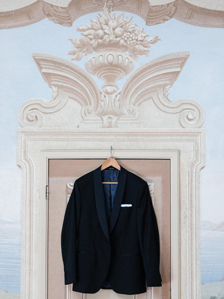 Navy groom suit hanging beneath ornate architectural details at La Foce wedding venue in Tuscany
