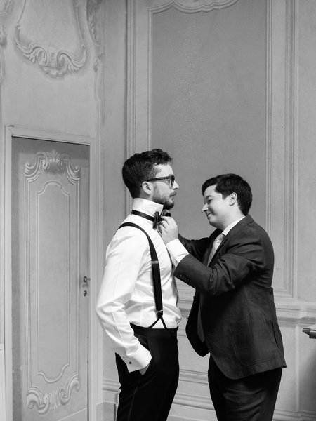 Black and white portrait of groom having his bow tie adjusted before ceremony in Tuscany