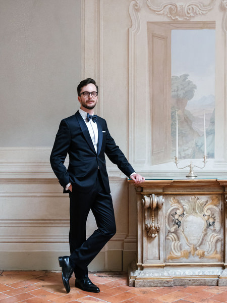 Groom in classic black tuxedo posing in historic Tuscan villa interior before ceremony