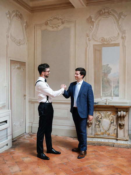 Groom greeting his best man inside ornate Renaissance hall at La Foce estate