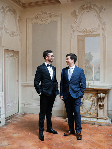Groom and groomsman standing beneath frescoed archways at La Foce in Tuscany