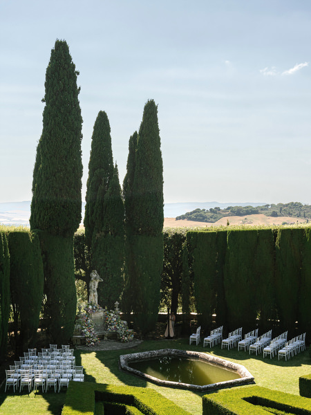 White ceremony chairs arranged beside manicured hedges in the Tuscan gardens of La Foce