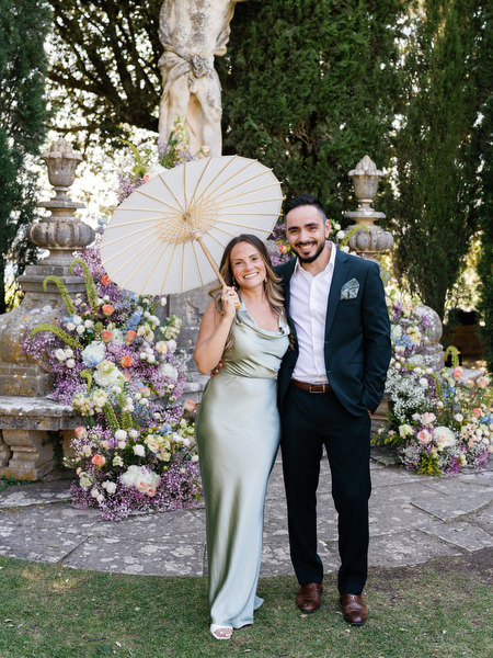 Elegant guest couple posing in front of floral ceremony backdrop at La Foce wedding in Tuscany