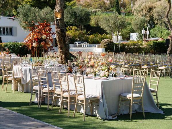 Reception tables arranged beneath Mediterranean trees at Island Resort the Residence for an Indian wedding in Athens