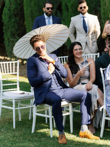 Guest holding parasol while seated at outdoor ceremony in the Tuscan gardens