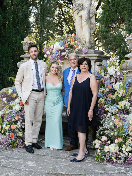 Family portrait in front of floral ceremony installation at La Foce wedding venue in Tuscany