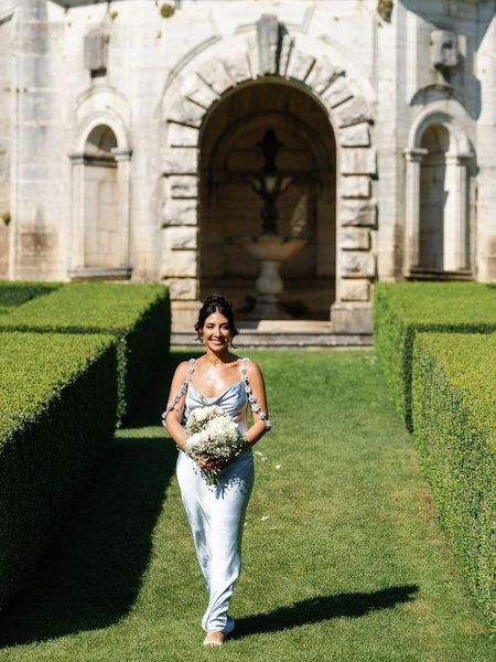 Bridesmaid carrying bouquet through the formal Italian gardens at La Foce