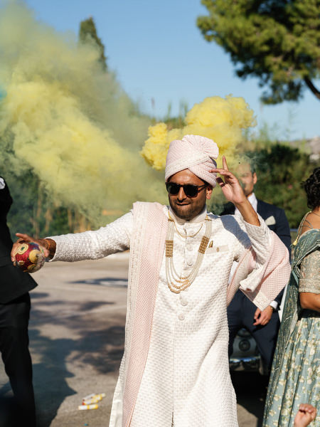 Groom dancing beneath yellow smoke during the baraat at Island Resort the Residence, Greece
