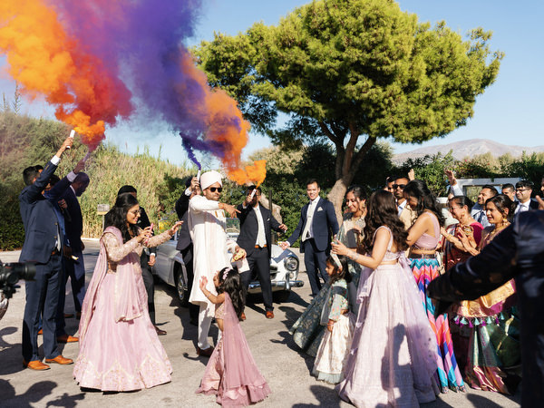 Groom surrounded by colorful smoke during their Indian wedding in Athens at Island Resort