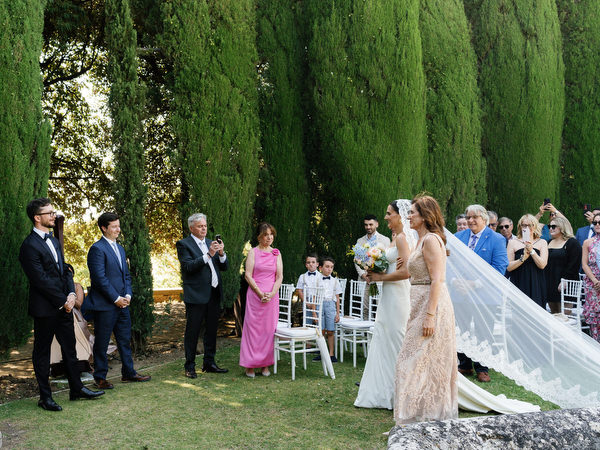 Bride arriving at outdoor garden ceremony at La Foce in Tuscany with cathedral veil flowing behind her
