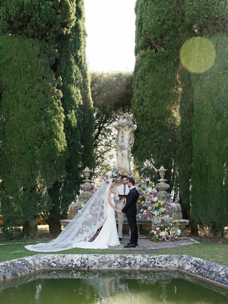 Bride and groom standing beneath floral ceremony installation at La Foce wedding in Tuscany