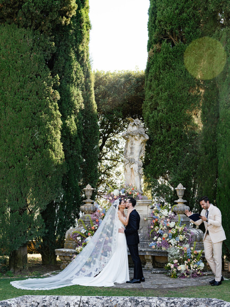 Bride and groom celebrating their first kiss beneath floral altar at La Foce in Tuscany