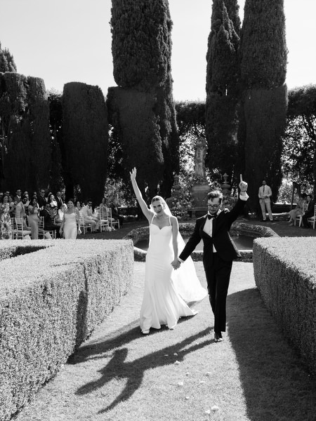 Bride and groom celebrating as they walk hand in hand through the gardens after ceremony in Tuscany