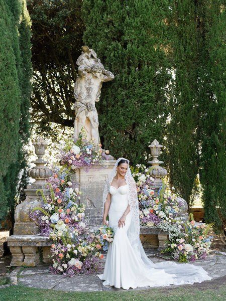 Bride in fitted gown walking past romantic floral arrangements in Italian garden setting
