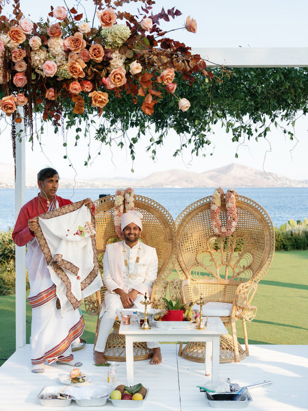 Groom seated beneath floral canopy on the mandap at Island Resort the Residence overlooking the Athens Riviera