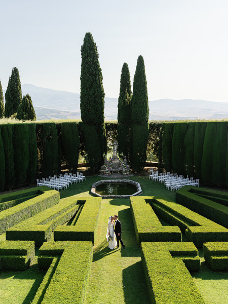 Bride and groom strolling through sunlit Italian gardens after ceremony at La Foce