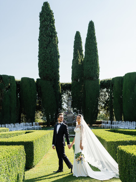 Bride and groom walking hand in hand through manicured Renaissance gardens at La Foce wedding