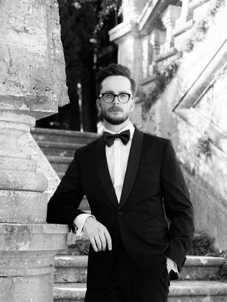 Black and white portrait of groom in tuxedo against historic stone staircase at La Foce in Tuscany