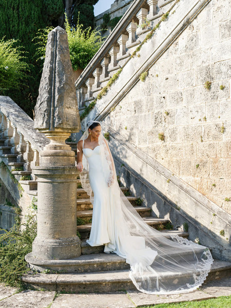 Bride in fitted gown descending the grand stone staircase at La Foce estate in Tuscany