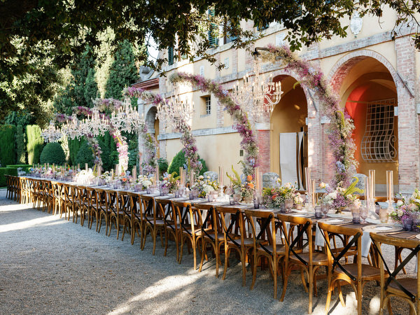 Long al fresco reception table with cascading floral arches at La Foce estate in Tuscany