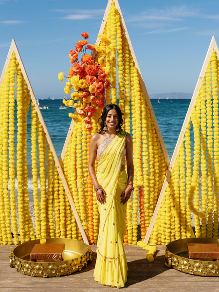 Bride posing in yellow Haldi outfit at beach ceremony