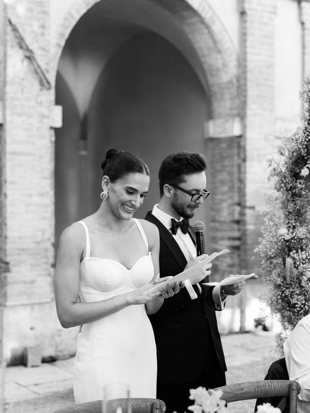 Black and white portrait of bride and groom reading speeches in historic Italian courtyard