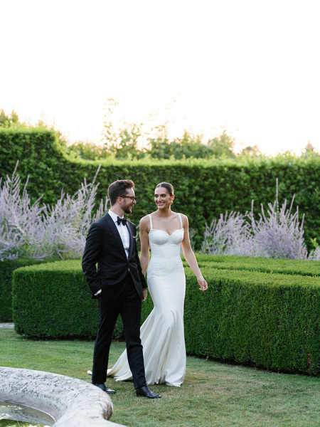 Bride and groom walking through Tuscan gardens during golden hour at luxury estate wedding