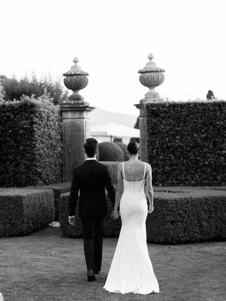 Bride and groom walking away hand in hand through formal Italian gardens