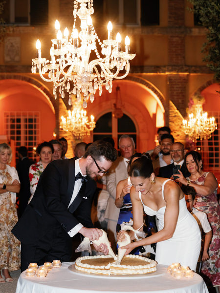 Romantic cake cutting moment during candlelit courtyard reception in Tuscany