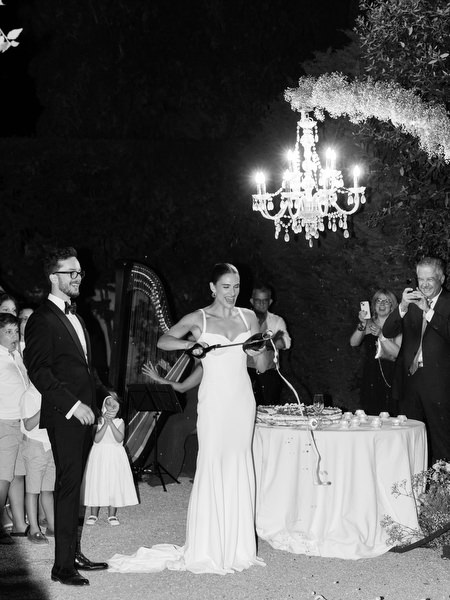 Black and white portrait of bride opening champagne during outdoor reception in Tuscany