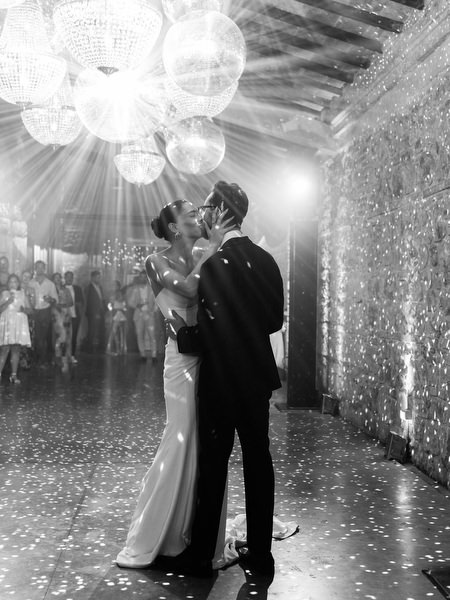 Timeless black and white portrait of newlyweds dancing under chandelier lighting