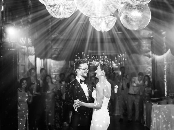 Timeless black and white portrait of newlyweds dancing under chandelier lighting