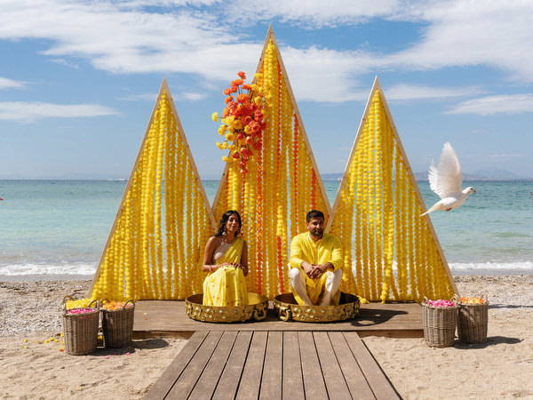 Couple seated at Haldi ceremony beach installation and a dove is flying