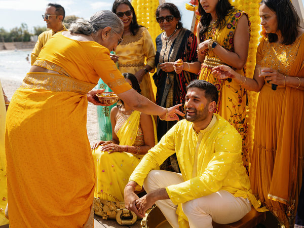Groom seated while friends apply Haldi turmeric