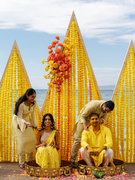 Bride and groom sitting while turmeric is applied during Haldi