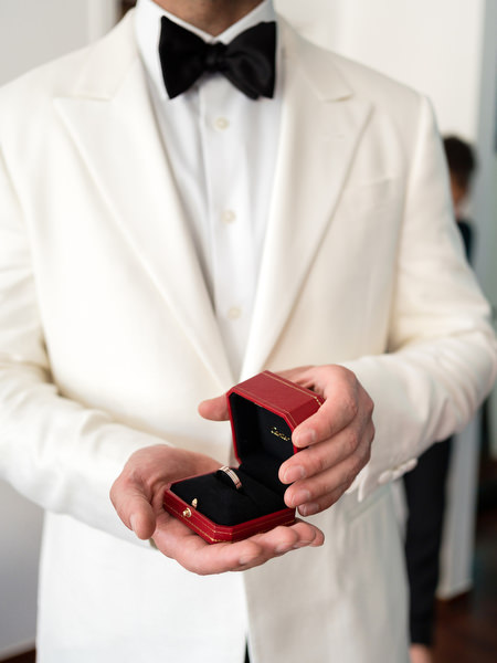 Groom in ivory tuxedo holding Cartier wedding rings in Athens.