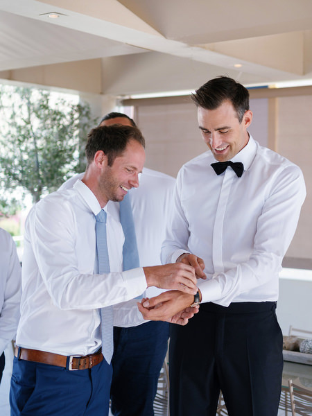 Groomsmen helping the groom get ready at Island Resort before a black-tie Athens Riviera wedding.