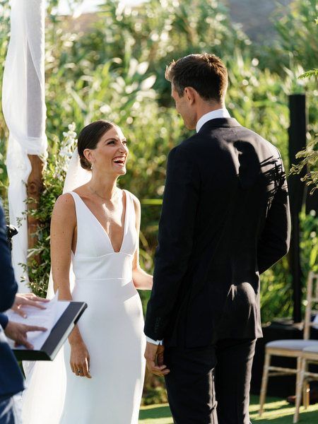 Bride and groom holding hands beneath chuppah at Island Resort, romantic Athens Riviera wedding ceremony.