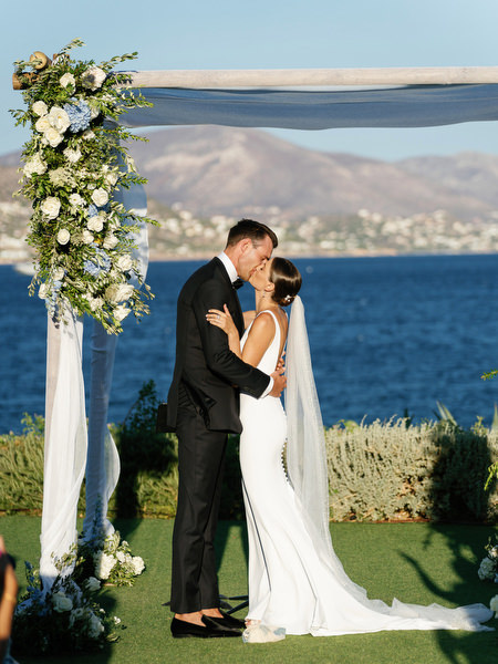 Bride and groom kissing beneath floral chuppah at Island Resort, seaside Athens Riviera Jewish wedding ceremony.