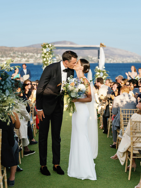 Bride and groom kissing during recessional at Island Resort, romantic seaside wedding in Athens, Greece.