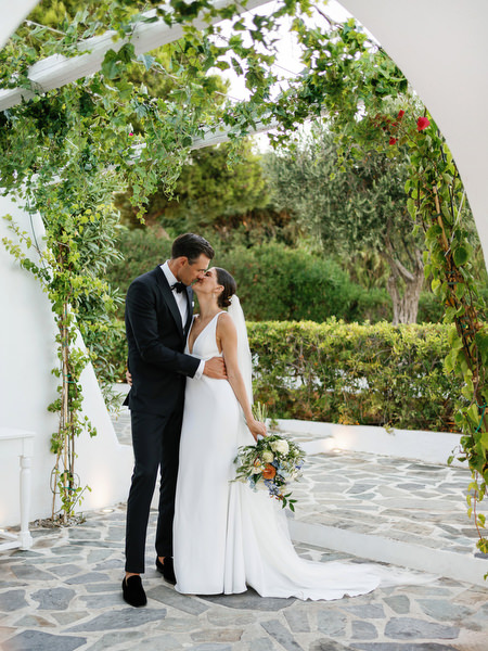 Bride and groom embracing under white arch at Island Resort, romantic Athens Riviera wedding in Greece.