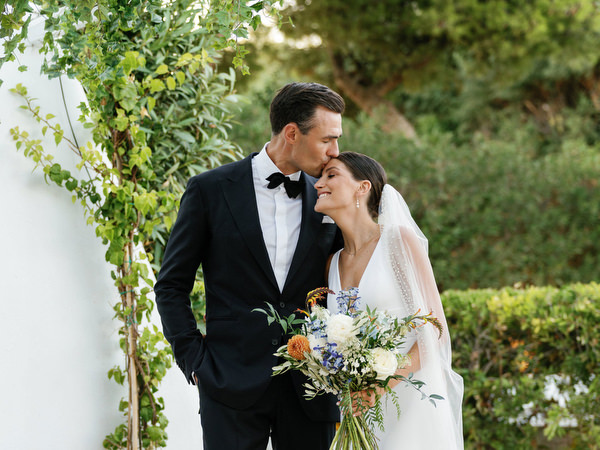 Groom kissing bride under vine-covered arch at Island Resort, romantic Athens Riviera seaside wedding.