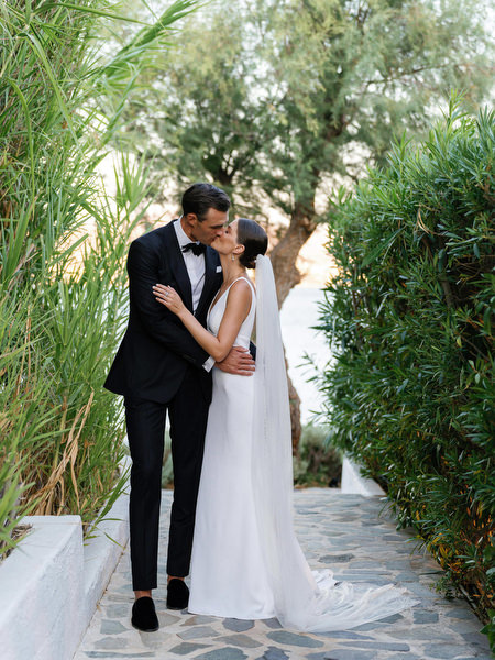 Bride and groom kissing along lush garden path at Island Resort, romantic Athens Riviera wedding in Greece.