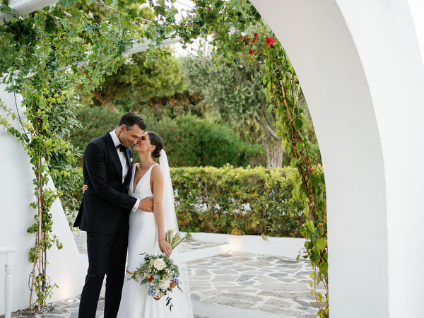 Bride and groom embracing under Mediterranean arch at Island Resort, romantic Athens destination wedding.