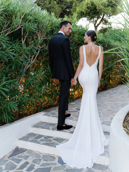 Groom kissing bride along garden path at Island Resort, romantic Athens Riviera wedding moment.