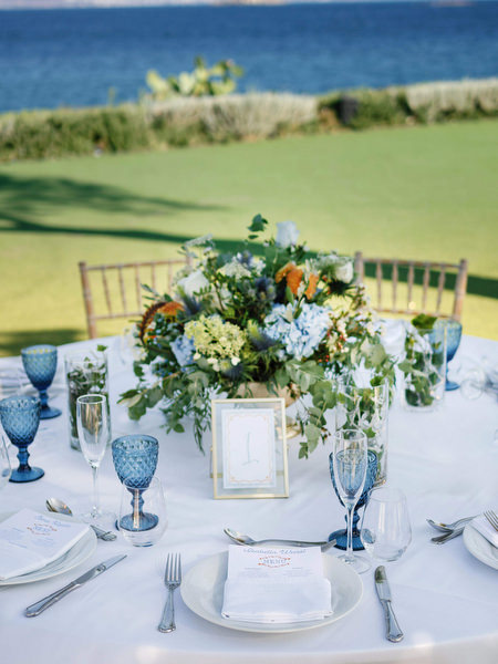 Reception floral centerpiece with blue glassware at Island Resort, elegant Athens wedding by the sea.